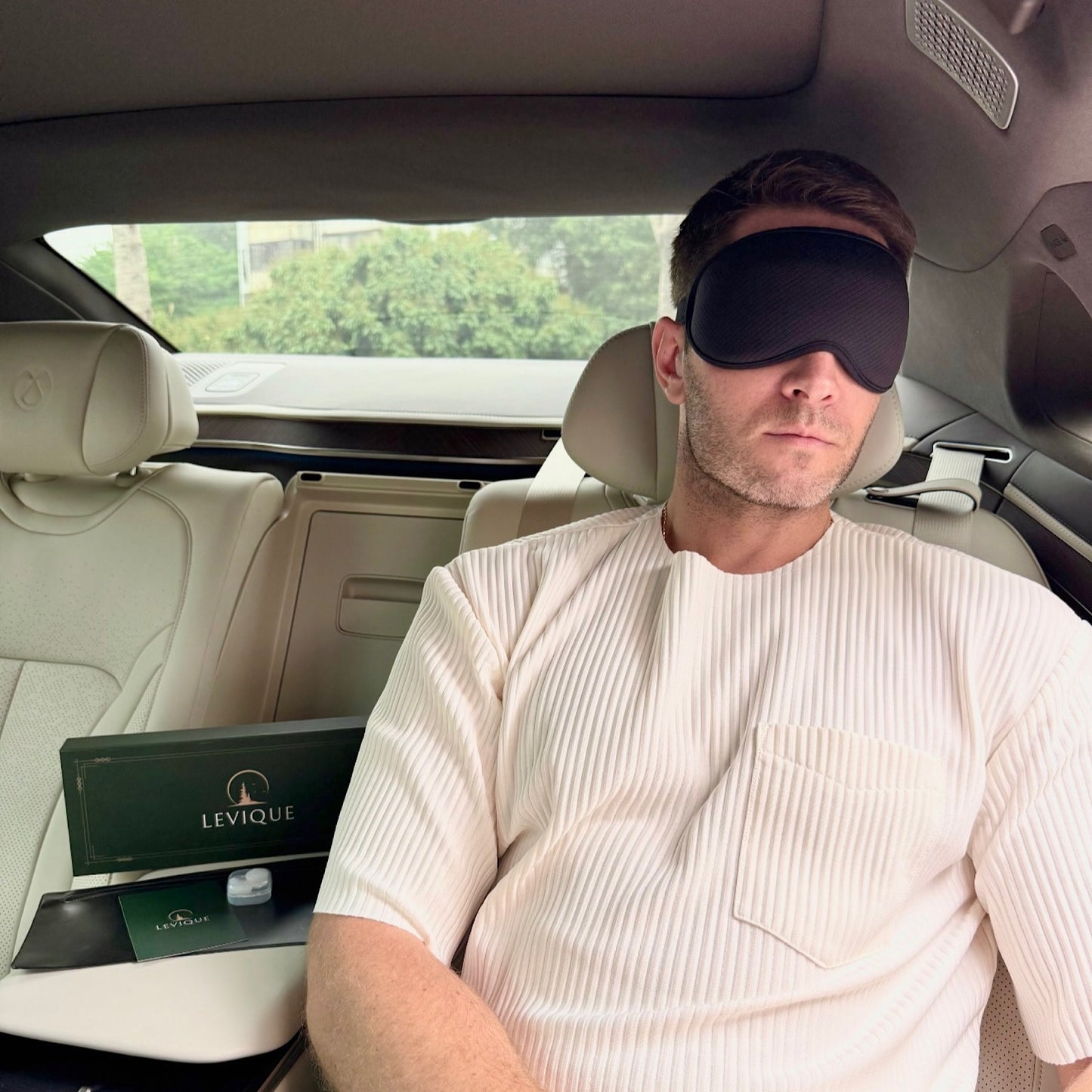 Man resting in car wearing LEVIQUE black 3D sleep mask, luxury travel accessory with premium gift set.
