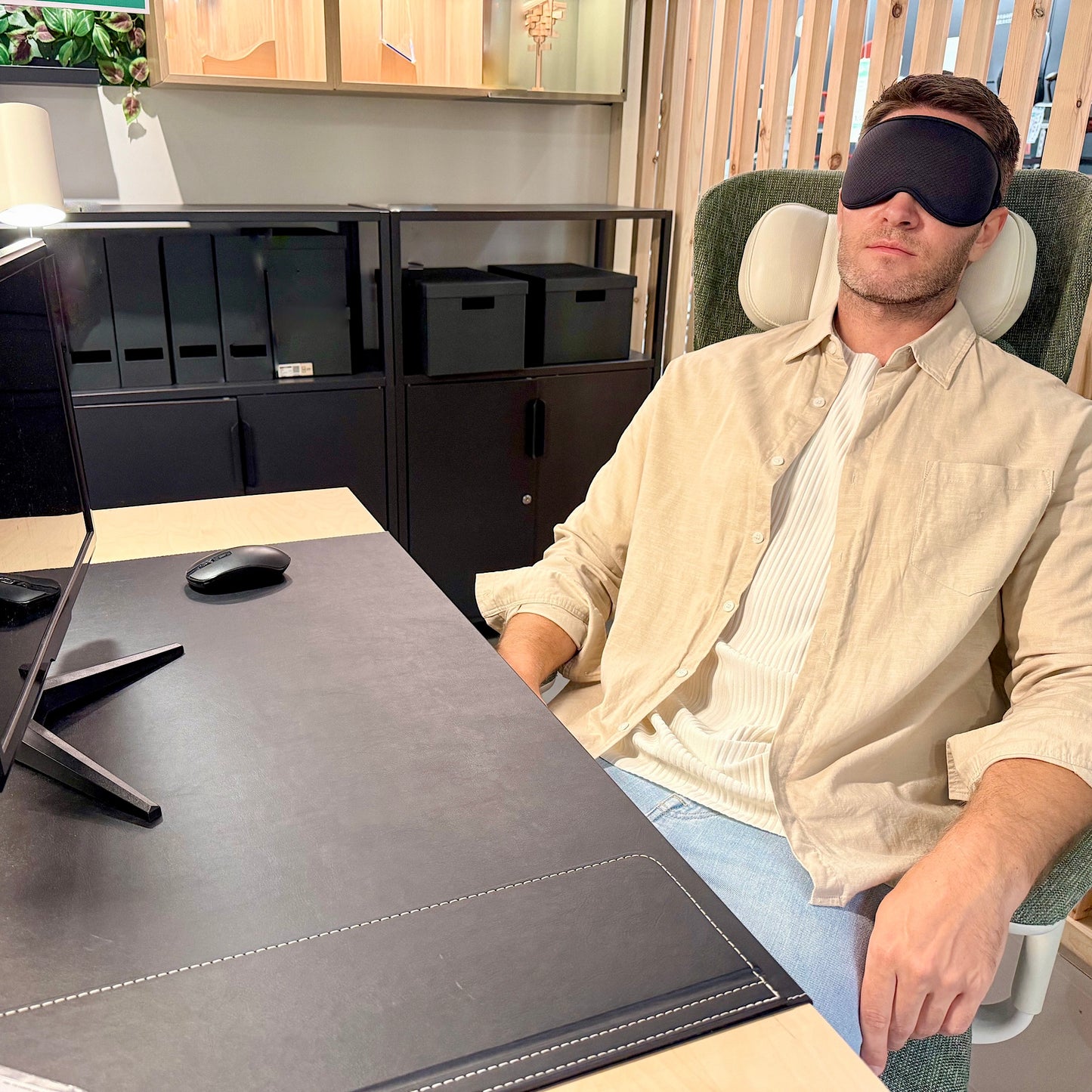 Man wearing LEVIQUE black 3D sleep mask while resting at office desk, ideal for power naps and stress relief during work.