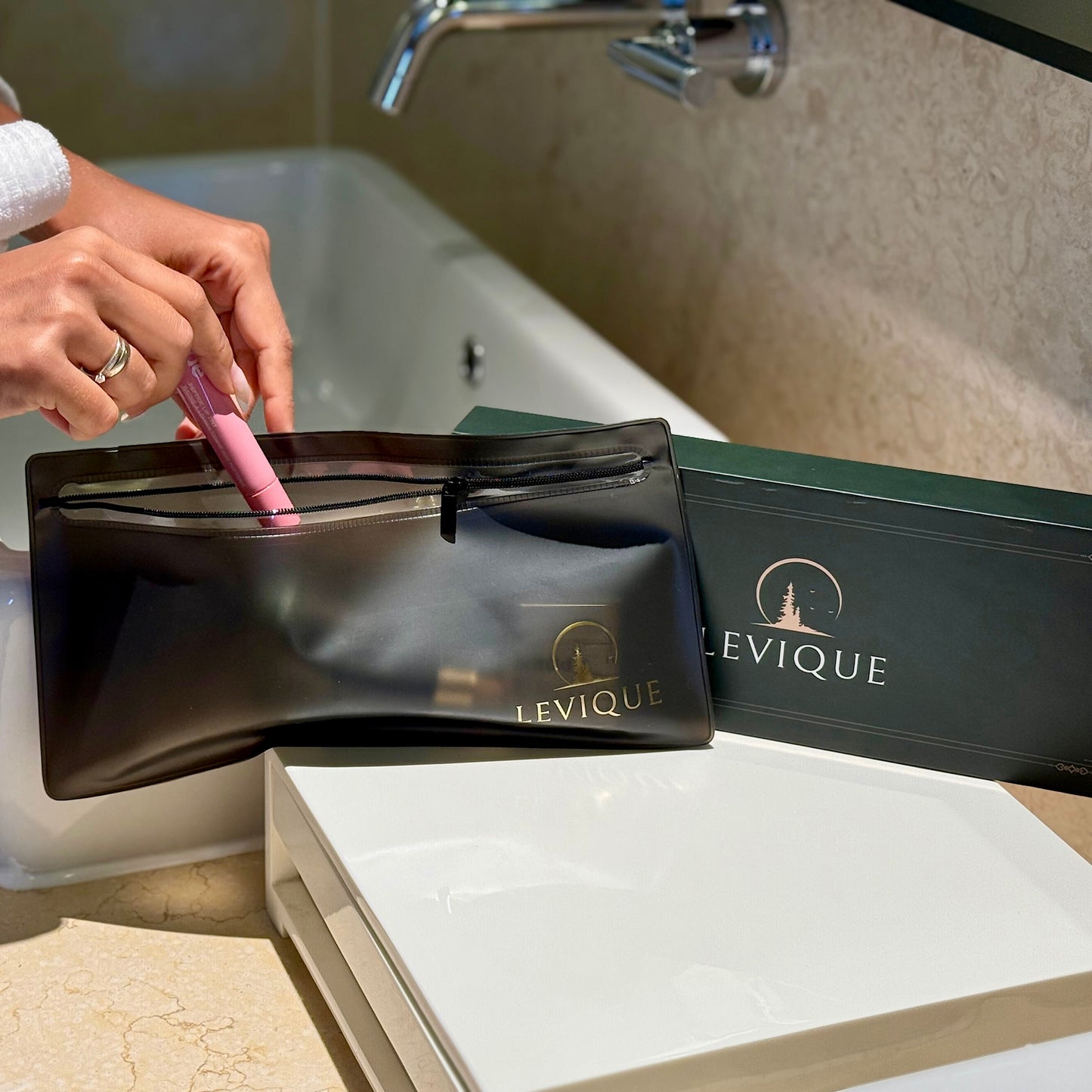 LEVIQUE Sweet Dreams Gift Set travel bag displayed in a bathroom with a person placing items inside, alongside the premium LEVIQUE gift box.