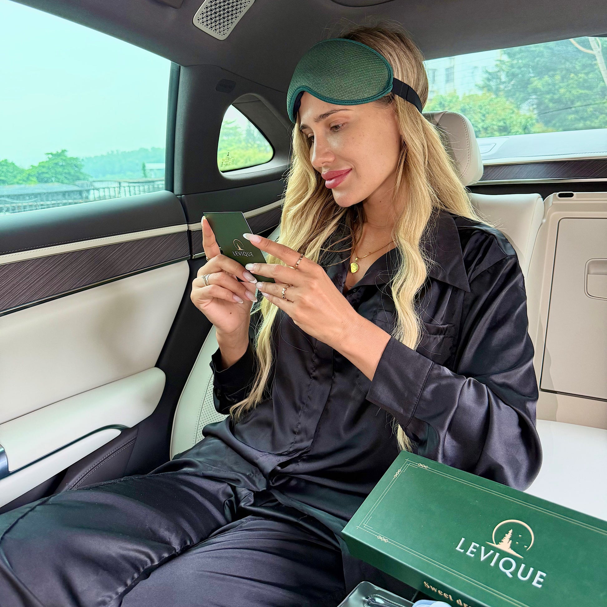 Woman in car wearing LEVIQUE green 3D sleep mask and reading bedtime affirmation card, premium travel gift set.